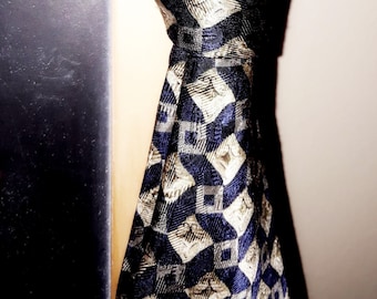 May include: A blue and white patterned tie with a geometric design. The tie is tied in a knot and hangs down.