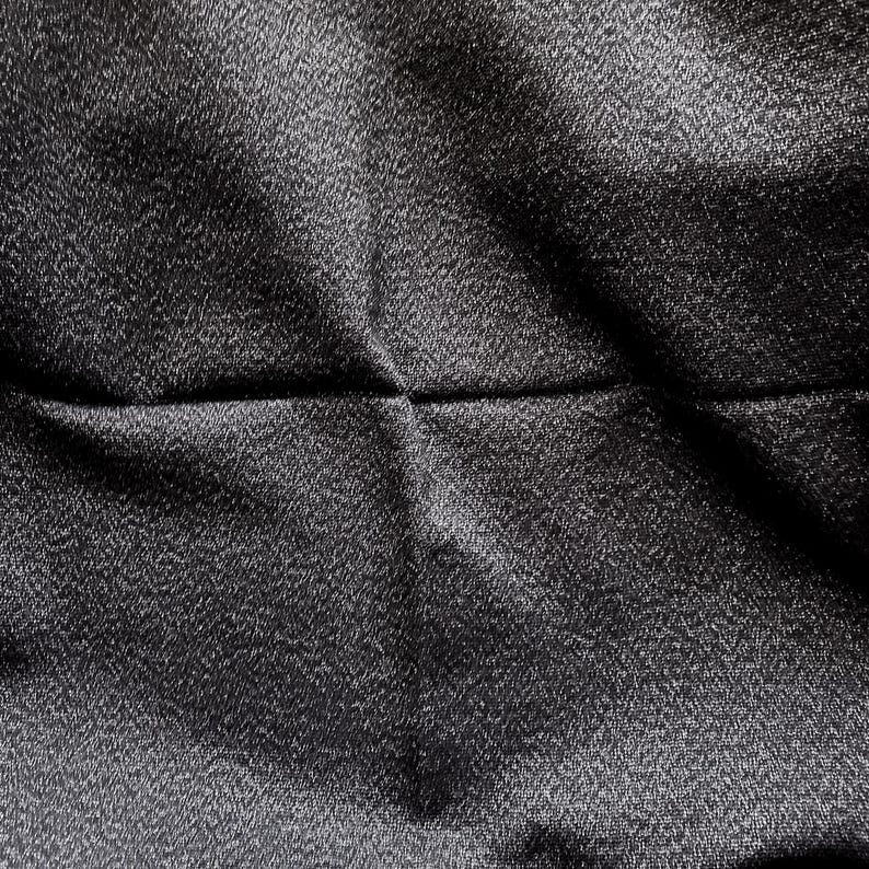 May include: Close-up of a dark gray fabric with a subtle sheen. The material has a textured surface with visible folds and creases, creating shadows and highlights. The fabric appears to be tightly woven.