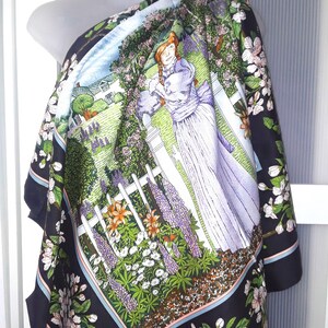 May include: A black silk scarf with a colorful floral print featuring a woman standing in a garden with a white picket fence. The scarf has a blue border and the text "Eleanor Paine" in the bottom right corner.