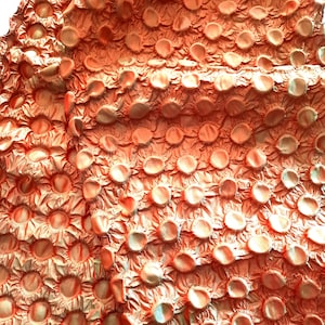 Puede incluir: Primer plano de una tela texturizada con un patrón de círculos en relieve. La tela es de color naranja melocotón y tiene un ligero brillo iridiscente.