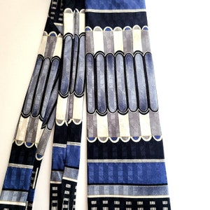 May include: A blue, grey, and white patterned silk tie. The tie has a geometric design with repeating shapes and lines.