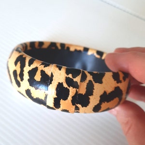 May include: A black and tan leopard print bangle bracelet. The bracelet is made of a hard plastic material and has a smooth, glossy finish.