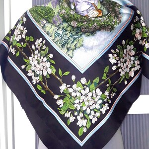 May include: A black silk scarf with a floral print of white blossoms and green leaves. The scarf has a blue and pink border.