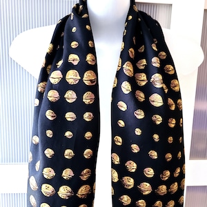 May include: A black silk scarf with a repeating pattern of gold walnuts. The scarf is folded in half and draped over a mannequin.