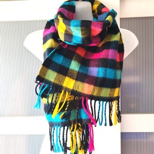 Peut inclure: Une écharpe à carreaux colorés avec des carrés noirs, jaunes, roses, bleus et verts. L'écharpe a des franges aux extrémités.