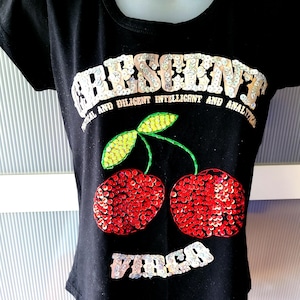 May include: Black t-shirt with a sequined design of a cherry and the text "Crescent" and "Virgo". The text below the cherry reads "Practical and Diligent, Intelligent and Analytical".