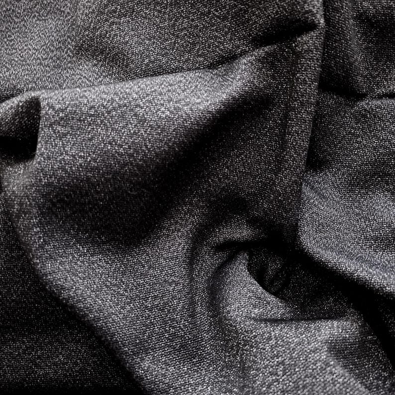 May include: Close-up of a dark gray fabric with a textured surface. The fabric is heavily draped, creating deep shadows and highlights. The material appears to be woven, with a subtle sheen. The overall effect is one of depth and richness.