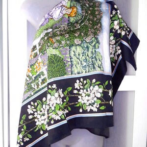May include: A black and white silk scarf with a floral design. The scarf features a woman sitting in a garden with flowers and trees. The scarf has a blue, white, and pink border.