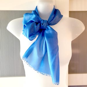 May include: A light blue silk scarf with a frayed edge. The scarf is tied in a knot around a white mannequin's neck.
