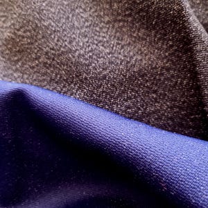 May include: Close-up of two fabric swatches. The top swatch is a dark gray, textured material. The bottom swatch is a deep blue, smooth fabric. The fabrics are layered, showcasing their contrasting textures and colors.