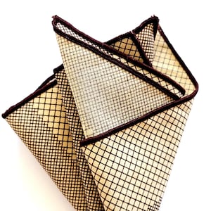 May include: A beige pocket square with a brown grid pattern and a brown border.