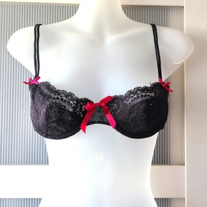 May include: A black lace bra with red ribbon accents. The bra has adjustable straps and a hook and eye closure in the back.
