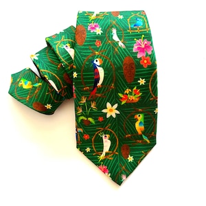 Puede incluir: Una corbata de seda verde con un estampado tropical con loros coloridos, flores y hojas. La corbata tiene un extremo puntiagudo y un patrón repetitivo.