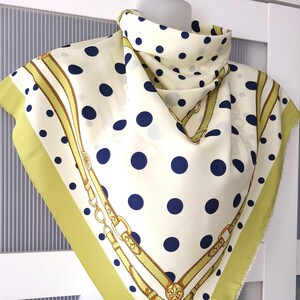 May include: A white silk scarf with a navy blue polka dot pattern and a gold chain design. The scarf has a green border.