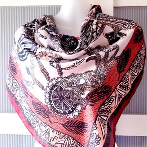May include: A square silk scarf with a detailed pattern. The scarf features a cream background with black and brown ornate designs, including chains, feathers, and geometric shapes. The border is a deep red, adding a contrasting frame to the overall design.