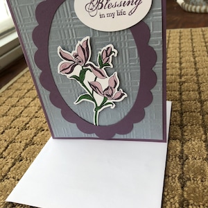 May include: A purple and gray card with a scalloped border and a white oval with the text "You are such a Blessing in my life". The card features a floral design with three pink flowers and green leaves.