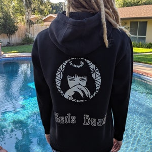 May include: Black hoodie featuring a white circular graphic of a woman's face and the text "Ted's Dead". The person is wearing patterned leggings and standing near a swimming pool.