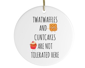 May include: White ceramic ornament with a gold string for hanging. The ornament features the text "TWATWAFFLES AND CUNTCAKES ARE NOT TOLERATED HERE" with cartoon waffle and cupcake illustrations.