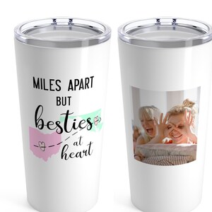 May include: Two white stainless steel tumblers with lids. One tumbler has the text "Miles Apart But Besties at Heart" with a pink and green heart graphic. The other tumbler has a photo of two people smiling.