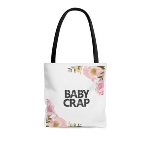 K&ouml;nnte beinhalten: Wei&szlig;e Einkaufstasche mit schwarzen Henkeln und einem Blumendesign. Der Text "BABY CRAP" ist in Schwarz auf die Tasche gedruckt.