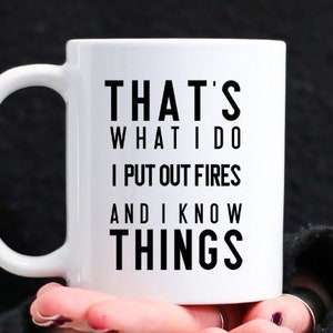May include: White ceramic coffee mug with black text that reads "That's what I do I put out fires and I know things".