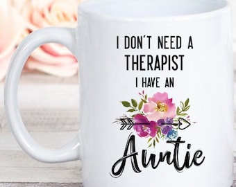 Könnte beinhalten: Weiße Keramik-Kaffeetasse mit einer schwarz-weißen Grafik, auf der "Ich brauche keinen Therapeuten, ich habe eine Tante" steht, mit einem Blumendesign und einem Pfeil.