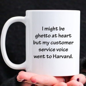 May include: White ceramic coffee mug with black text that reads "I might be ghetto at heart but my customer service voice went to Harvard."