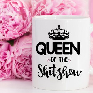 May include: White ceramic mug with a black crown and the text "Queen of the Shit Show" in black with two pink hearts.