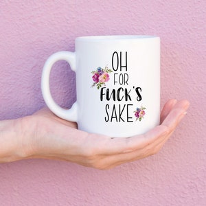 K&ouml;nnte beinhalten: Wei&szlig;e Keramik-Kaffeetasse mit schwarzem Blumendesign und dem Text "OH FOR FUCK'S SAKE".