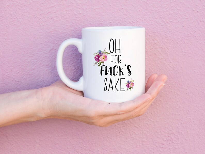 K&ouml;nnte beinhalten: Wei&szlig;e Keramik-Kaffeetasse mit schwarzem Blumendesign und dem Text "OH FOR FUCK'S SAKE".