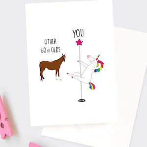 May include: A greeting card with a white unicorn holding a pole and a brown horse. The text on the card reads "You" above the unicorn and "Other 60-yr olds" above the horse.