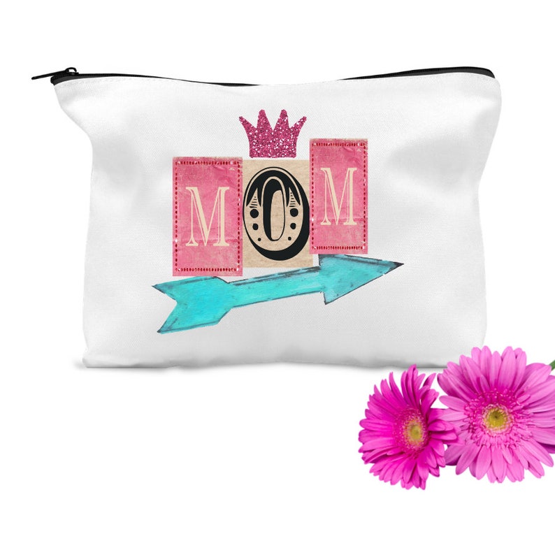K&ouml;nnte beinhalten: Wei&szlig;e Rei&szlig;verschlusstasche mit einer rosa Krone und dem Wort "MOM" in rosa und wei&szlig;en Bl&ouml;cken mit einem Hufeisen in der Mitte. Ein blauer Pfeil zeigt nach rechts.