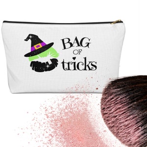 May include: White zippered makeup bag with a black witch hat and a green face with a black beard. The text "Bag of tricks" is printed in black.