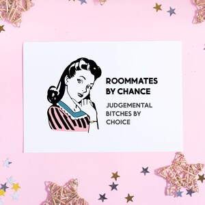 May include: A white card with a black and white illustration of a woman with a pink and black striped shirt. The text on the card reads "Roommates by chance, Judgemental Bitches by choice."
