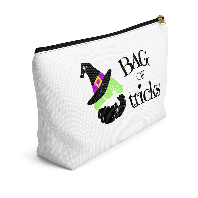 May include: White zippered pouch with a black and green witch's hat and the text "Bag of tricks" in black.