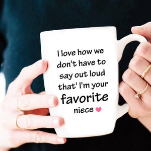 May include: White ceramic mug with a black handle and the text "I love how we don't have to say out loud that I'm your favorite niece" with a pink heart.