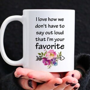 May include: White ceramic mug with a black text saying "I love how we don't have to say out loud that I'm your favorite" and a floral design with an arrow.