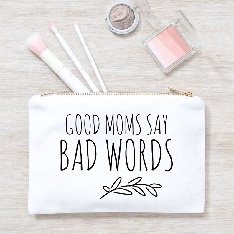 Puede incluir: Bolsa de maquillaje de lona blanca con cremallera dorada. La bolsa tiene texto negro que dice "Good Moms Say Bad Words" con un peque&ntilde;o dise&ntilde;o floral negro debajo del texto.
