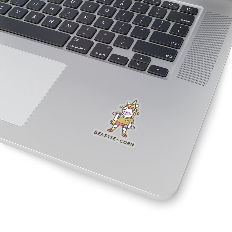 May include: A sticker featuring a cartoon unicorn with a rainbow horn, wearing a pink shirt and holding pink dumbbells. The unicorn is sweating and has a happy expression. The text "BEASTIE-CORN" is below the unicorn.