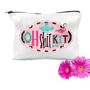 K&ouml;nnte beinhalten: Wei&szlig;e Canvas-Kosmetiktasche mit einem rosafarbenen ovalen Design, das den Text "OH SHIT KIT" in schwarzer und rosa Schrift zeigt. Ein t&uuml;rkisfarbener Kronleuchter und ein rosa Flamingo sind ebenfalls im Design enthalten.