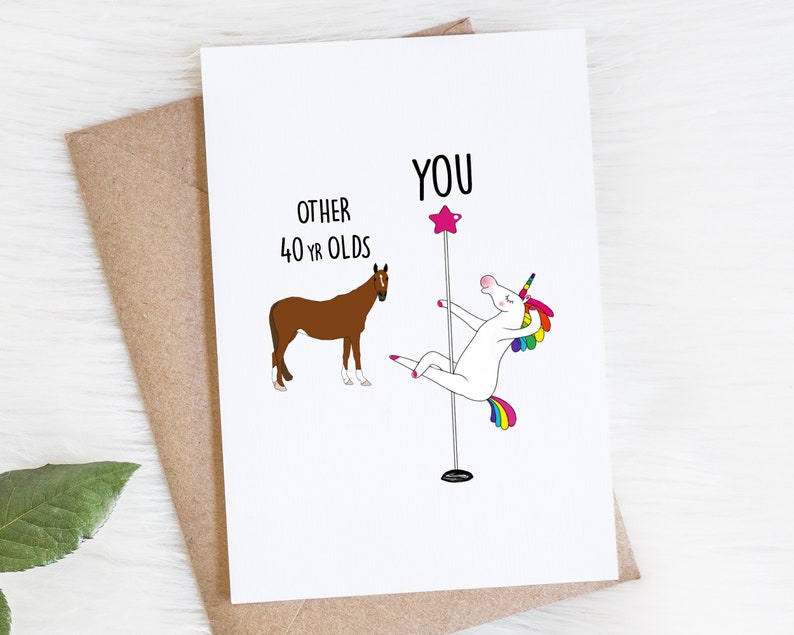 K&ouml;nnte beinhalten: Eine Gru&szlig;karte mit einem wei&szlig;en Einhorn, das auf einer Stange mit einem rosa Stern oben tanzt. Der Text "YOU" befindet sich &uuml;ber dem Einhorn. Der Text "OTHER 40 YR OLDS" steht neben einem braunen Pferd.