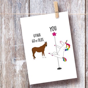 May include: A humorous birthday card featuring a white unicorn with a rainbow tail and mane, dancing on a pole, with the text "YOU" above it. A brown horse is shown on the left side of the card with the text "OTHER 60 YR OLDS" above it.