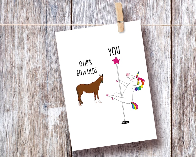 May include: A humorous birthday card featuring a white unicorn with a rainbow tail and mane, dancing on a pole, with the text "YOU" above it. A brown horse is shown on the left side of the card with the text "OTHER 60 YR OLDS" above it.