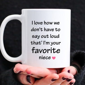 May include: White ceramic coffee mug with a black inscription that reads "I love how we don't have to say out loud that I'm your favorite niece" with a pink heart.