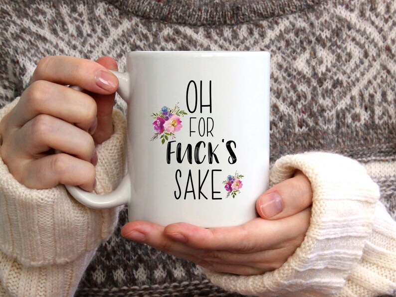 K&ouml;nnte beinhalten: Eine wei&szlig;e Keramiktasse mit einem schwarzen Blumendesign und dem Text "OH FOR FUCK'S SAKE".