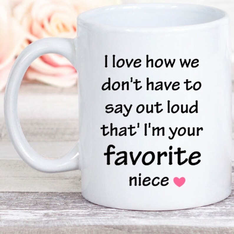 May include: White ceramic mug with a black inscription that reads "I love how we don't have to say out loud that I'm your favorite niece" with a pink heart.