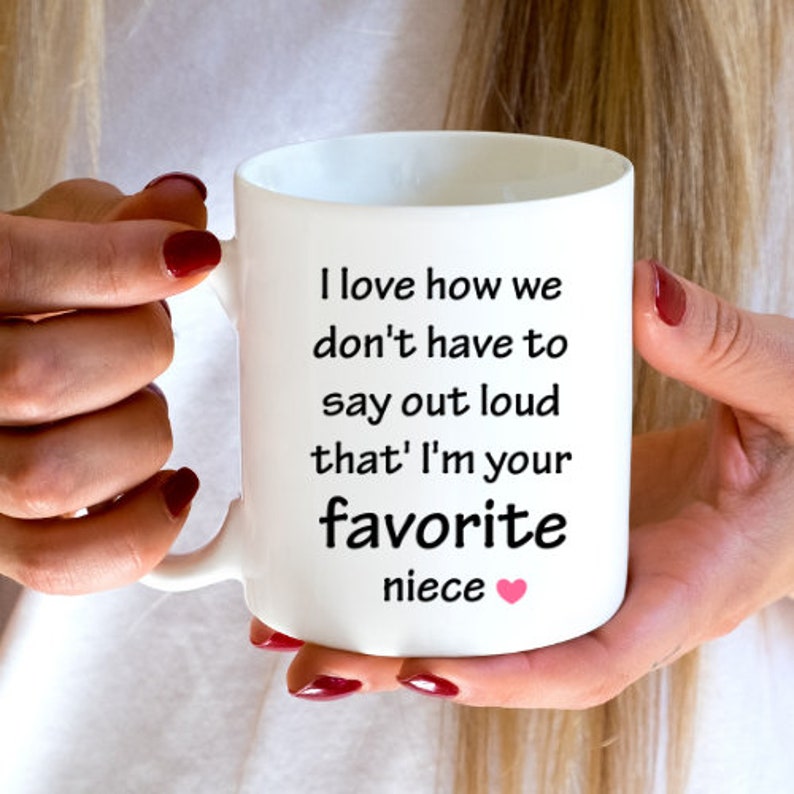 May include: White ceramic mug with a black inscription that reads "I love how we don't have to say out loud that I'm your favorite niece" with a pink heart.