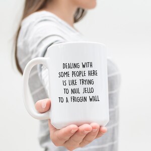 Może przedstawiać: Biały ceramiczny kubek z dużym uchwytem. Kubek ma czarny tekst, kt&oacute;ry brzmi: "DEALING WITH SOME PEOPLE HERE IS LIKE TRYING TO NAIL JELLO TO A FRIGGIN WALL."