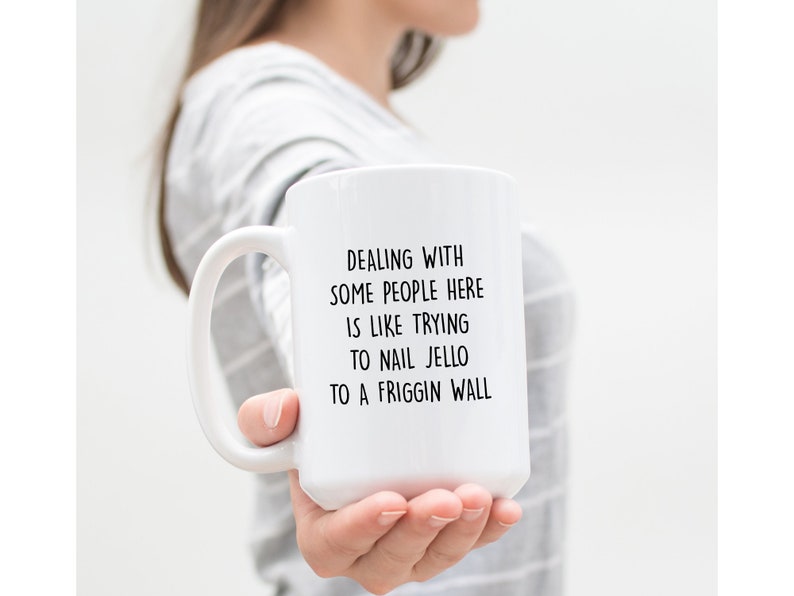 Może przedstawiać: Biały ceramiczny kubek z dużym uchwytem. Kubek ma czarny tekst, kt&oacute;ry brzmi: "DEALING WITH SOME PEOPLE HERE IS LIKE TRYING TO NAIL JELLO TO A FRIGGIN WALL."
