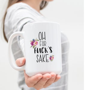 K&ouml;nnte beinhalten: Wei&szlig;e Keramik-Kaffeetasse mit schwarzem Blumendesign und dem Text "OH FOR FUCK'S SAKE".